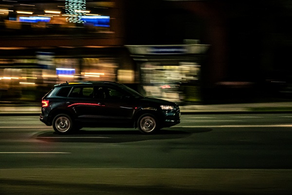 Black SUV speeding down a city street at night with blurred lights in the background.